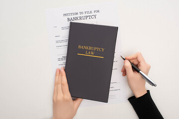 cropped view of woman with bankruptcy paper, law book and pen on white background