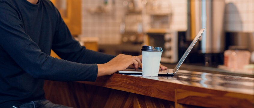 Young asian man drinking coffee in cafe and using laptop computer. Freelancer working from coffee shop