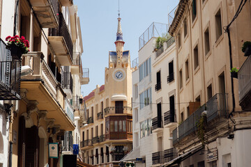 Fototapeta na wymiar Urban street with clock on chapel and blue sky at background in Catalonia, Spain