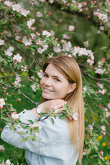 Fototapeta premium Girl in a flowering garden. A young blond woman is walking in a park. Portrait of a beautiful girl in the park.