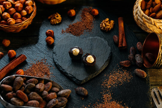 Cut handmade chocolate candy with haselnut on blackstone stand in heart shape. Chocolate candies with cocoa beans, nuts, cocoa powder around
