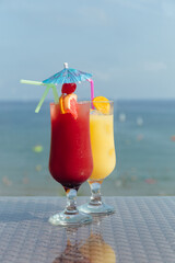 Two glasses of cocktails with drinking straws on table and sea with sky at background