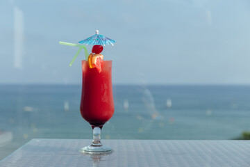 Glass of cocktail with cocktail umbrella and drinking straws on table with sea and blue sky at background