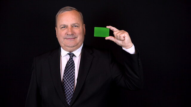Old businessman in a suit holds a bank card in his hand. Chromakey green card. Isolated black background. 4k