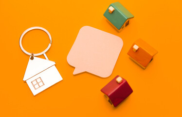 Metal keychain in the form of a house and toy houses on a orange background