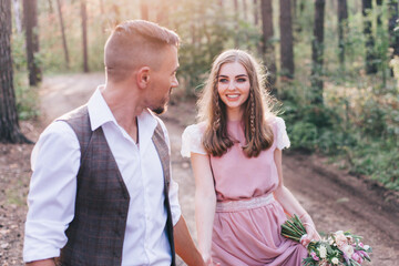 Beautiful couple at the photoshoot of love story in the forest in a rustic dress