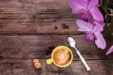 Obraz na płótnie Canvas Cup of coffee on wooden table with coffee beans and amaretti, orchid in background