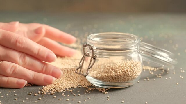 White raw quinoa, South American grain, female hands pour seeds into glass jar. Healthy and gluten free food.
