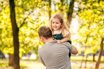  dad with a small daughter are playing in the park on the street, a toddler is sitting on his fathers shoulders, close-up, the child is laughing, concept happy fathers day.