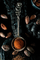 Handmade chocolate candies lay on cocoa powder in spoon on smut. Truffles lay on charcoal on blackstone stand.