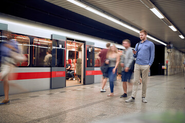 young relaxed man in a subway, not in a hurry, looking at his cell phone, texting, reading, sending, message, email