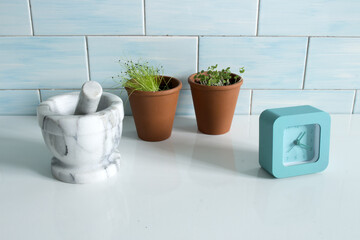 Terracotta pots with a small light blue table clock and a grey marble mortar on white tabl and ceramic blue wall.