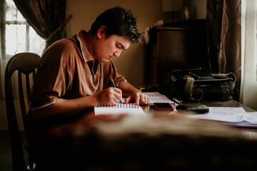 A young Asian man sitting at his desk and and taking note