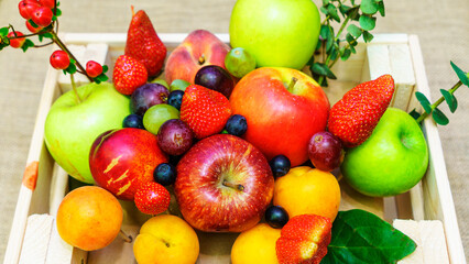 Set of berries and fruits in wooden box. Apple, strawberry, grape, berry and peach on a red brick...