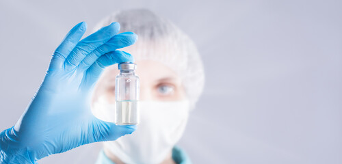 Doctor holding a vial of transparent liquid. Scientist looks at a bottle of vaccine.