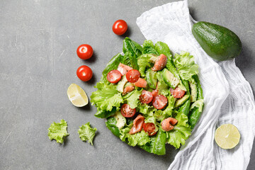Salmon salad with avocado, green leaves, tomatoes on gray background