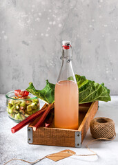 Glass bottle of homemade rhubarb syrup  in a wooden box with green leaves. Healthy summer food...