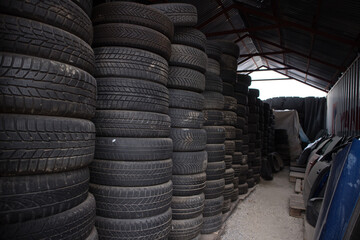 Obraz premium A lot of used and worn tires from cars one on top of each other. Also, some automobile doors. Inside a warehouse. At a vehicle graveyard. For recycle or re-sale. Kozani. Greece.
