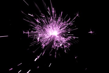 Fototapeta premium Pink sparkler countdown on fire with spread of glitter sparks. Luxury entertainment at e.g. New Years Eve, Independence Day or birthday party celebration. Glowing light spark on dark background