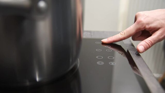 Close up woman hand turns on induction kitchen stove.