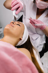 Obraz na płótnie Canvas Woman receiving cleansing therapy with a professional ultrasonic equipment in cosmetology office