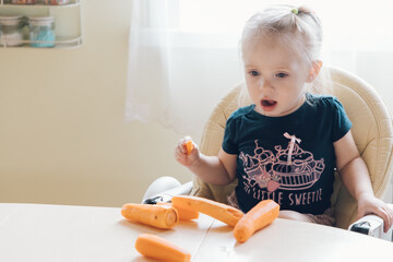 Little girl sits on a table and eats a carrot