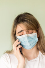 young woman with blond hair wearing a blue face mask and a white t-shirt calling through her gray...
