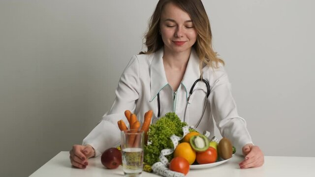 Diet and health. A female doctor of Caucasian appearance sits at a table and looks at vegetables and fruits
