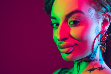 Close up portrait of young caucasian woman on purple studio background in neon light. Beautiful female model with tattoos. Human emotions, facial expression, sales, ad concept. Freak's culture.