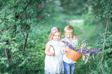 A girl in a white dress hugs a boy who is holding a basket of flowers. Children's interaction