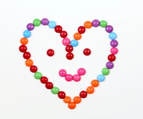 Smiling heart made from colored smarties. Chocolate candies in a shape of heart with smile on face, white background,