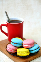 Colorful french Sweet Pastries Macaroons on glass table and red coffee mug on wooden tray.