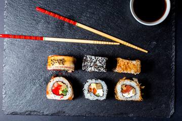 sushi maki roll with sesame and soy sauce with chopsticks on a dark plate.
