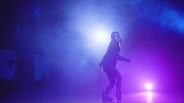 Sudden appearance from smoke of an attractive roller skate girl doing various complex elements and turns in closed dark area in abandoned building against brick wall. Experienced woman rollerblading.