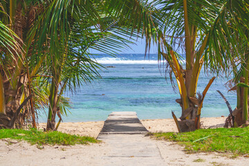 Beautiful beach with a small wooden path in the Philippines with blue cloudy sky and palm trees