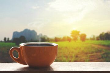 Hot Black hot coffee with smoke. Ceramic brown glass placed on an outdoor wood table. The background is a landscape of nature with mountains and farmland with vintage colors. Business ideas