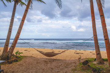 Beautiful beach in the Philippines with blue cloudy sky, palm trees and a hammock