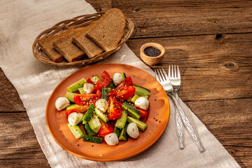 Fresh salad from tomato, cucumber and baby mozzarella. Sunny lunch with crusty bread