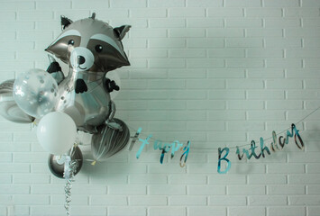 Birthday balloons: raccoon and black and white balloons against a white brick wall background
