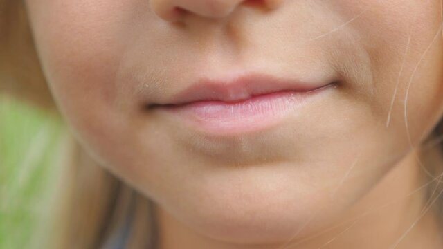 Close up lips of small cute girl with blonde hair smiling with mouth closed. Portrait of beautiful kid with glad expression on face. Detail view on happy child face. Front view Slow motion