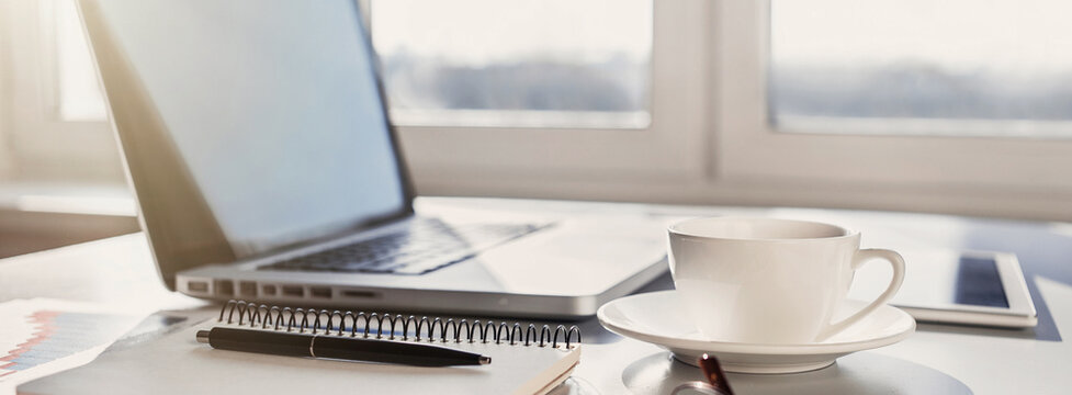 Workplace, laptop computer, coffee cup and notebook at office desk, panoramic banner. Business, technology, place of work, home office concept