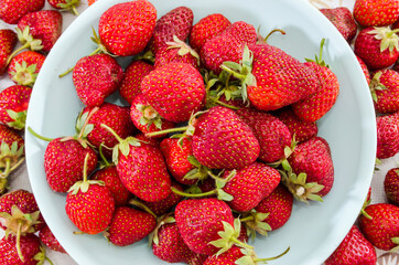 a lot of tasty strawberries in a plate on a background of strawberries. View from above. Close-up.