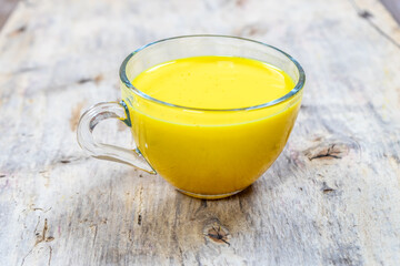 Golden milk in a glass cup on a wooden background
