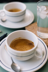 Two cups of delicious hot espresso coffee  on the green table background, standing along with glass of ice cold water, pen, paper notebook and sunglasses