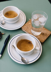 Two cups of delicious hot espresso coffee  on the green table background, standing along with glass of ice cold water, pen, paper notebook and sunglasses
