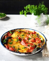 Baked fish (shark) with tomatoes and spices in a baking dish on a gray background, still life