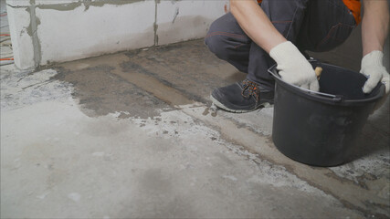 A worker wets a concrete floor with a brush for further waterproofing. Primer of a concrete floor before laying tiles on it, the final preparatory stage for strengthening the surface