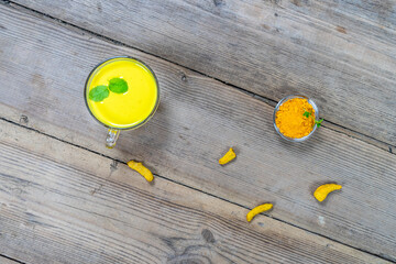 Golden milk in a glass cup on a wooden background