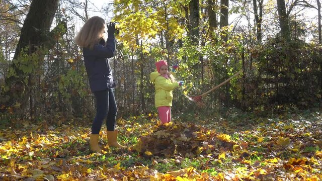 Young mother with little cute daughter throws autumn leaves up in air