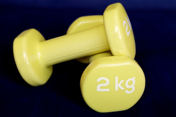 Yellow dumbbells for fitness weighing 2 kg over a dark blue background